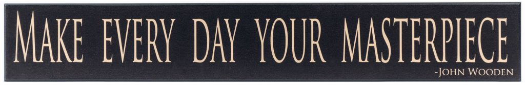 Black wooden sign with saying, "Make every day your masterpiece" in tan through the middle of the sign. John Wooden in the bottom right corner.